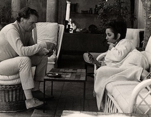 Actors Richard Burton (wearing white turtleneck and slacks) and Elizabeth Taylor (wearing caftan from Givenchy boutique), seated and lounging and playing gin while on vacation at La Fiorentina, Saint-Jean-Cap-Ferrat, 1967